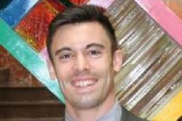 Gregory Mack smiling with colorful sculpture in the background