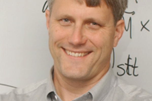 Mark D. Stiles smiling with whiteboard in the background