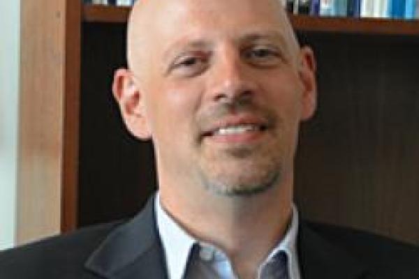Benn Tannenbaum smiling with wood bookshelf behind him