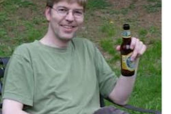 A picture of Joerg Bewersdorf sitting outdoors with a glass bottle beverage.