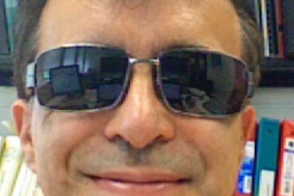 Piers Coleman in sunglasses with bookshelf behind him
