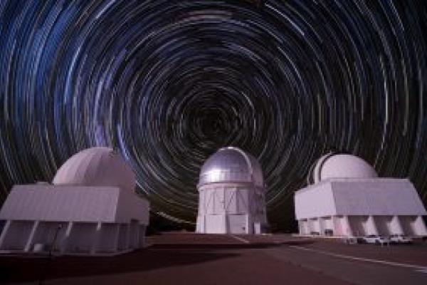 Three large white telescopes with sky swirling behind them