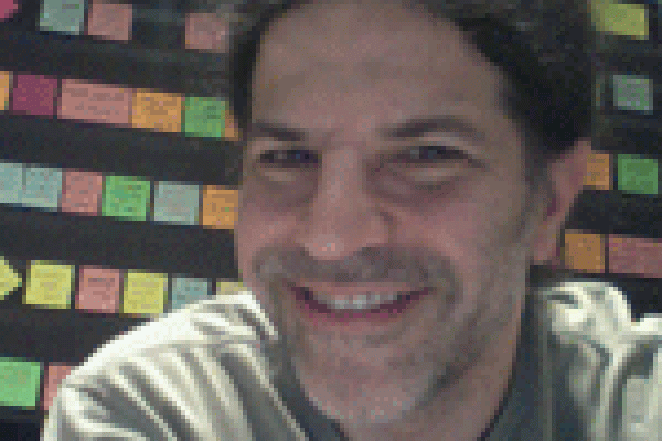 David Kaplan smiling with rows of sticky notes on wall behind him
