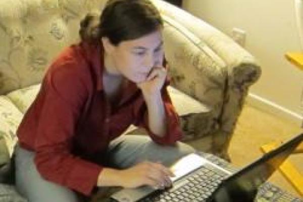An image of Linda Carpenter sitting on a couch, focused on what they are looking at on their computer.