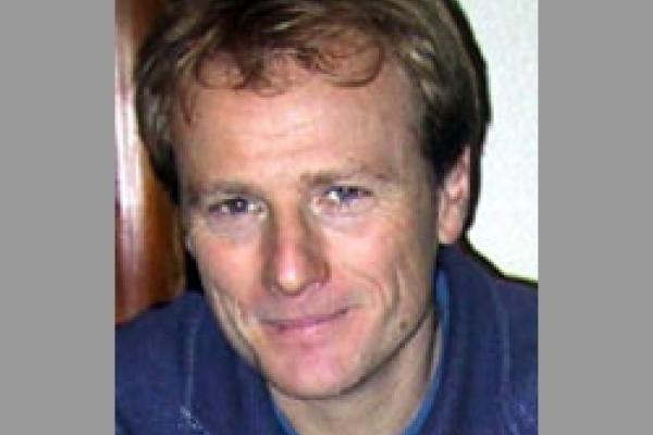 Morten Hjorth-Jensen pictured in front of a white wall. He has light brown hair and no facial hair, and he is wearing a blue collared shirt.