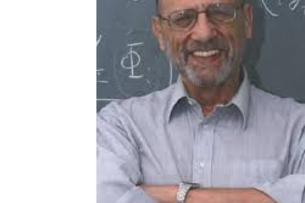 H.R. Reiss smiling with arms folded and standing in front of a chalkboard