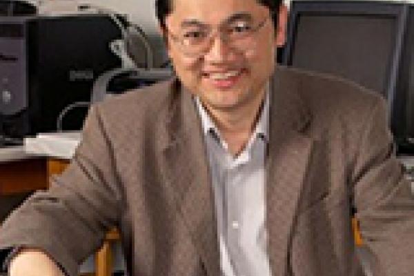 Dongping sitting on chair and smiling with computers in the background