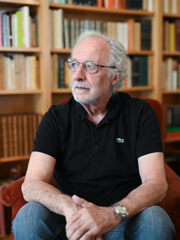 Photo of Pierre Agostini seated with blurred bookshelf behind him