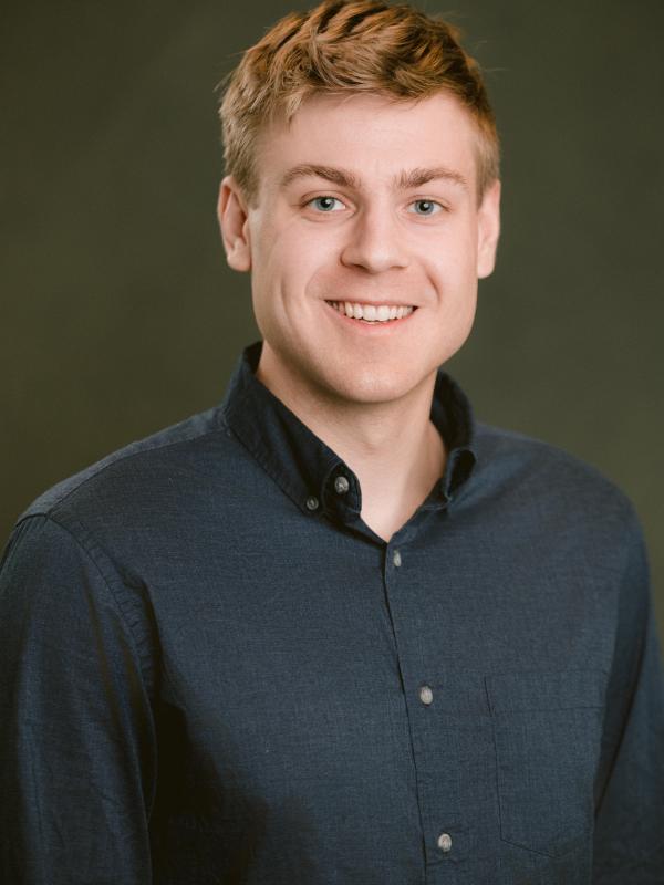 Man in his mid-twenties, with blonde hair, smiling towards the camera.