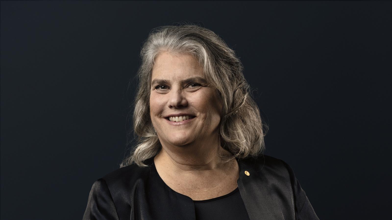 Andrea Ghez against plain black background with one hand on hip